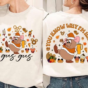 May include: White sweatshirt featuring a cartoon mouse character, Gus Gus, in a Santa hat and orange vest. The front design includes the text "gus gus" in a script font, surrounded by fall-themed graphics. The back has the text "YOU KNOW WHY I'M HERE".
