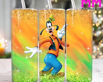 May include: A stainless steel tumbler featuring a vibrant design of Goofy from Disney. The tumbler has a straw and a colorful background with orange, green, and gold glitter accents. The design includes the text "MUSEMADESHOP".