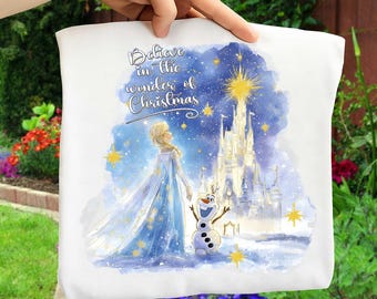 May include: White fabric featuring a watercolor illustration of a winter scene with a castle, a woman in a blue dress, and a snowman. The text "Believe in the wonder of Christmas" is written in script.