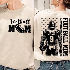 K&ouml;nnte beinhalten: Ein beiger Pullover mit dem Text "Football Mom" und einer Fu&szlig;ballabbildung auf der Vorderseite. Die R&uuml;ckseite des Pullovers zeigt einen Fu&szlig;ballspieler mit dem Text "Football Mom" und der Nummer "9" auf dem Trikot.