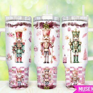 May include: Three stainless steel tumblers with lids and handles. Each tumbler features a different watercolor illustration of a nutcracker with a pink and white checkered background. The nutcrackers are dressed in red, green, and blue.