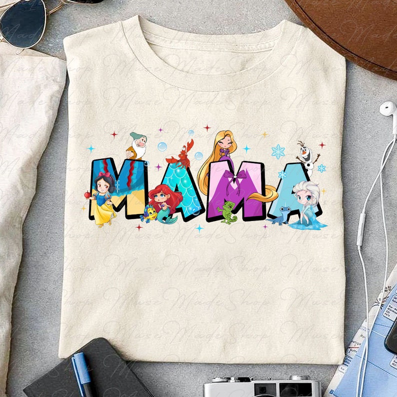 May include: A beige t-shirt with a graphic print of the word "MAMA" in colorful letters. Each letter is decorated with a different Disney princess character, including Snow White, Ariel, Rapunzel, and Elsa.