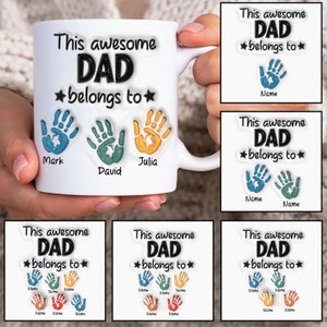 May include: White ceramic mug with the text "This awesome DAD belongs to" and three handprints with names "Mark", "David", and "Julia".