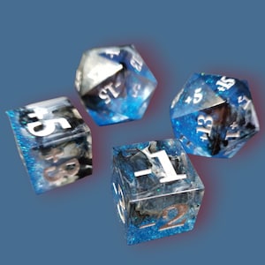 Könnte beinhalten: Vier polyedrische Würfel mit blauem, schwarzem und weißem Marmoreffekt. Die Würfel haben silberne und kupferfarbene Zahlen. Die Würfel sind für Rollenspiele.