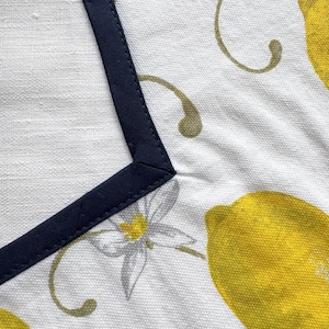 May include: White fabric with a navy blue border and a lemon and floral pattern. The design features bright yellow lemons, gray flowers, and olive green vines. The navy border frames the top left corner of the fabric.
