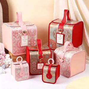 Puede incluir: Una colección de cajas de regalo decorativas en varios tamaños y colores. Las cajas presentan un diseño estampado con detalles en rosa, rojo y dorado. Cada caja tiene un asa y una etiqueta que dice "THANK YOU".