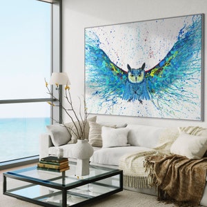 May include: A blue and green owl with its wings spread wide, painted in a splatter style on a white canvas. The owl's eyes are yellow and its beak is orange. The background is white with splashes of blue, green, and yellow paint.