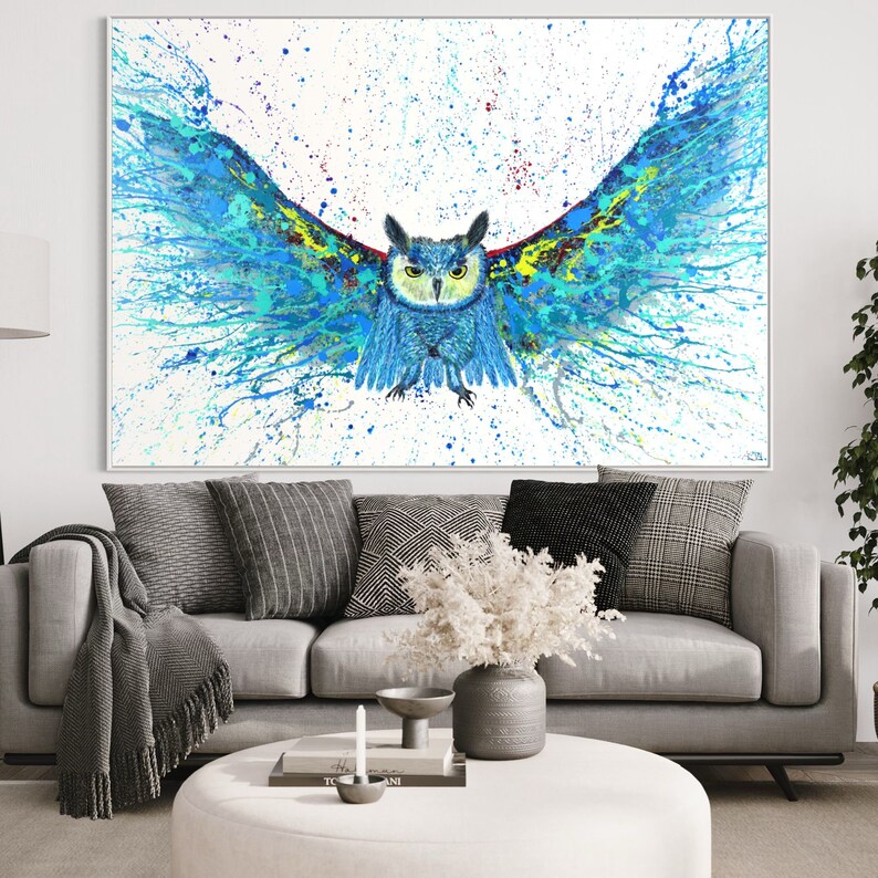 May include: A blue and green owl with its wings spread wide, painted in a splatter style on a white background. The owl's eyes are black and yellow, and its beak is orange. The painting is framed in a white frame.