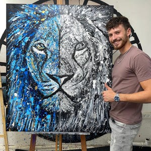 以下が含まれることがあります： 片側が青、もう片側が白のライオンの顔を描いた大きな抽象画。絵はキャンバスに描かれており、人が持っている。
