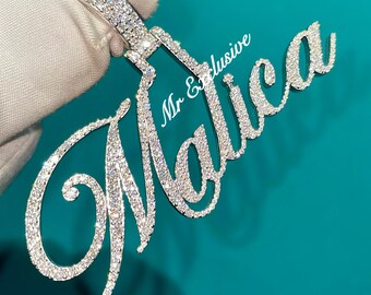 May include: A diamond-encrusted pendant spelling out the name "Malica" in a cursive font. The pendant is held against a teal background. The words "Mr & Exclusive" are also visible.