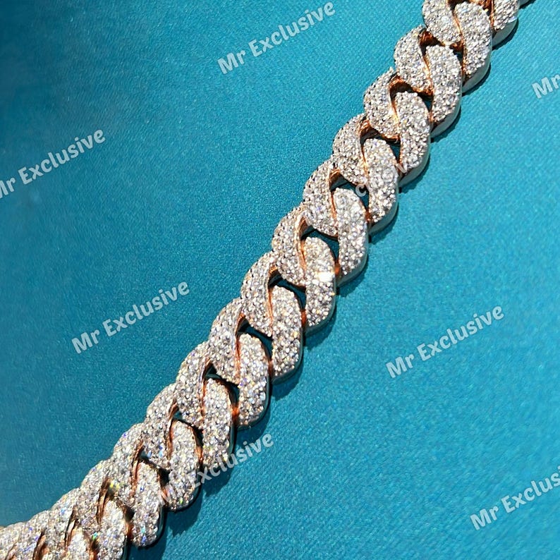 May include: A close-up of a gold-toned chain necklace with numerous embedded clear crystals. The chain has a curb link design. The background is a solid teal color. The text "Mr Exclusive" is visible in the background.