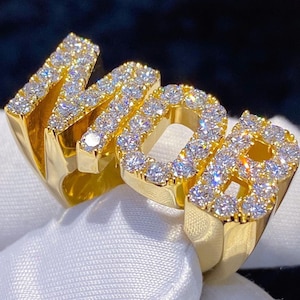 May include: A gold ring with the word "MOB" spelled out in large, raised letters. The letters are covered in small, clear diamonds.