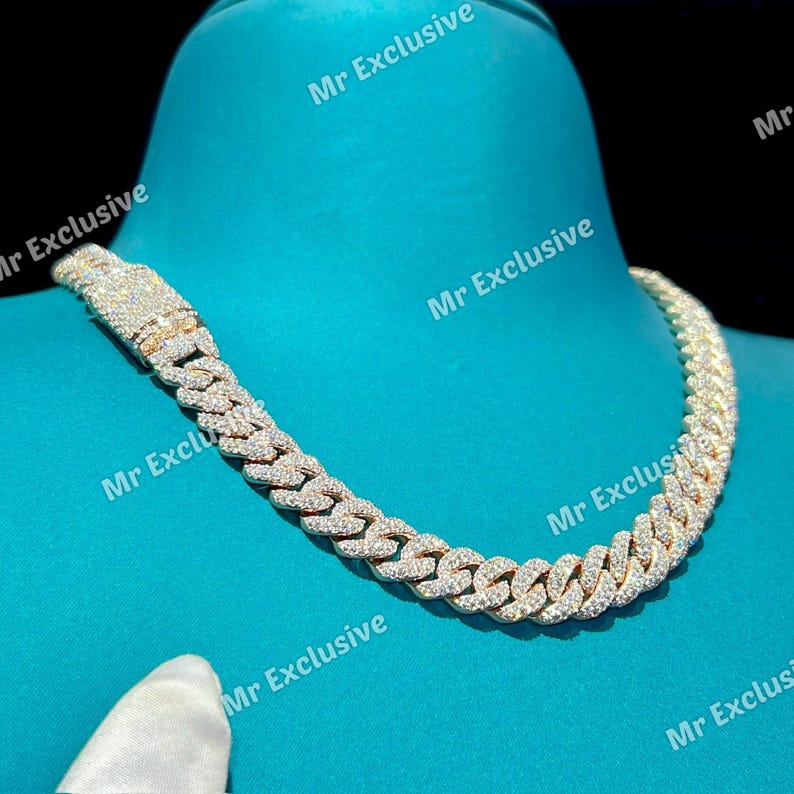 May include: A gold-toned, diamond-studded Cuban link chain necklace. The necklace is displayed on a blue surface. The text "Mr Exclusive" is watermarked across the image.