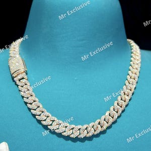 May include: A gold-toned cuban link chain necklace encrusted with sparkling, clear gemstones. The necklace has a secure clasp and is displayed on a teal background. The text "Mr Exclusive" is visible.