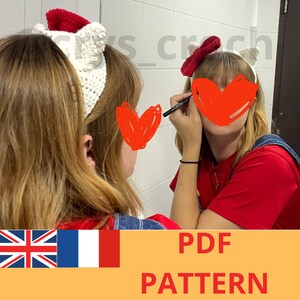 May include: A crochet headband with red and white accents. The headband is in the shape of a cat's ears. The headband is being worn by a person in a red shirt and blue overalls. The text "PDF PATTERN" is visible at the bottom of the image.