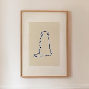 May include: A framed art print featuring a minimalist blue line drawing of a dog. The artwork is set against a cream-colored background and is enclosed in a natural wood frame. The print is mounted on a white wall.