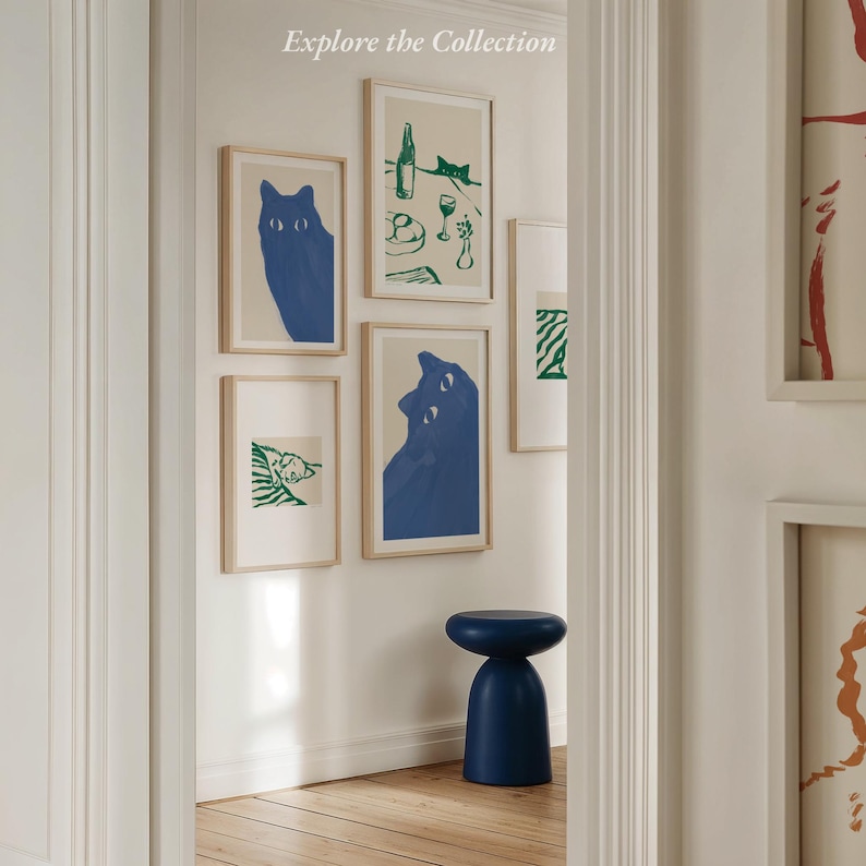 May include: A collection of framed art prints featuring blue cat illustrations and green line drawings. The prints are displayed on a white wall, with a blue stool in the foreground. The text "Explore the Collection" is at the top.