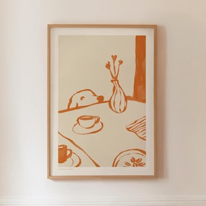 May include: A framed art print featuring an orange and cream illustration. The artwork depicts a dog peeking over a table set with a cup and saucer, a vase of flowers, and a plate. The style is minimalist and modern.