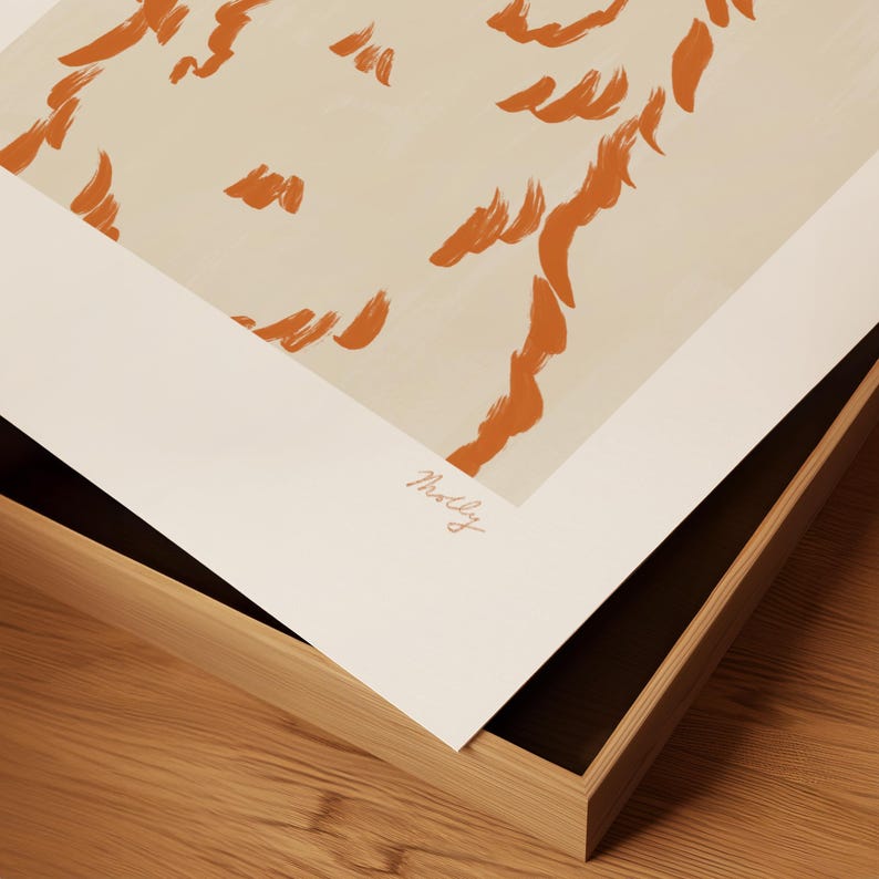 May include: Abstract art print with orange brushstrokes on a cream background, presented in a wooden frame. The artist's signature is visible. The print is angled, showing the frame's construction. The frame is made of wood.