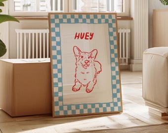 May include: A framed print featuring a red illustration of a smiling corgi dog with the name "HUEY" above it. The print has a white background with a blue and white checkered border. The frame is a light brown color.