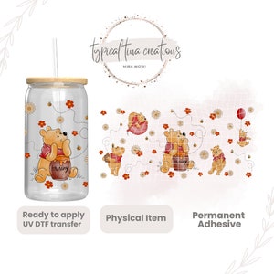 May include: A clear glass tumbler with a wooden lid and straw, decorated with a Winnie the Pooh design. The design includes Pooh Bear with a honey pot, flowers, and bees. The word "Hunny" is on the honey pot. The tumbler is decorated with a UV DTF transfer.