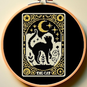 May include: A black and gold cross-stitch embroidery hoop with a black cat design and the text "THE CAT".