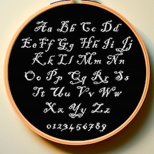 May include: A black embroidery hoop with white cursive letters spelling out the alphabet and numbers 0-9.