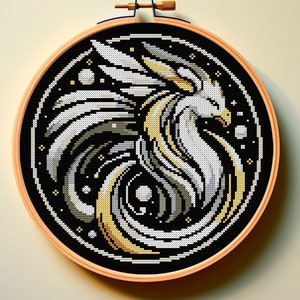 Può includere: Un cerchio da ricamo a punto croce nero e bianco con un design di drago stilizzato bianco e oro su sfondo nero. Il drago è circondato da stelle bianche e un motivo a spirale.