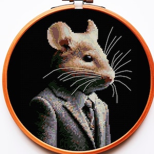Peut inclure: Une souris brune et blanche portant un costume gris avec une cravate noire. La souris est brodée sur un fond noir et encadrée dans un cercle en bois.