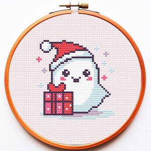 Könnte beinhalten: Ein weißer Geist, der einen roten Weihnachtsmann-Hut trägt und eine rote und weiße Geschenkbox mit rosa Punkten hält. Der Geist hat einen rosa Rouge und schwarze Augen. Der Hintergrund ist hellrosa mit blauen und violetten Schneeflocken.