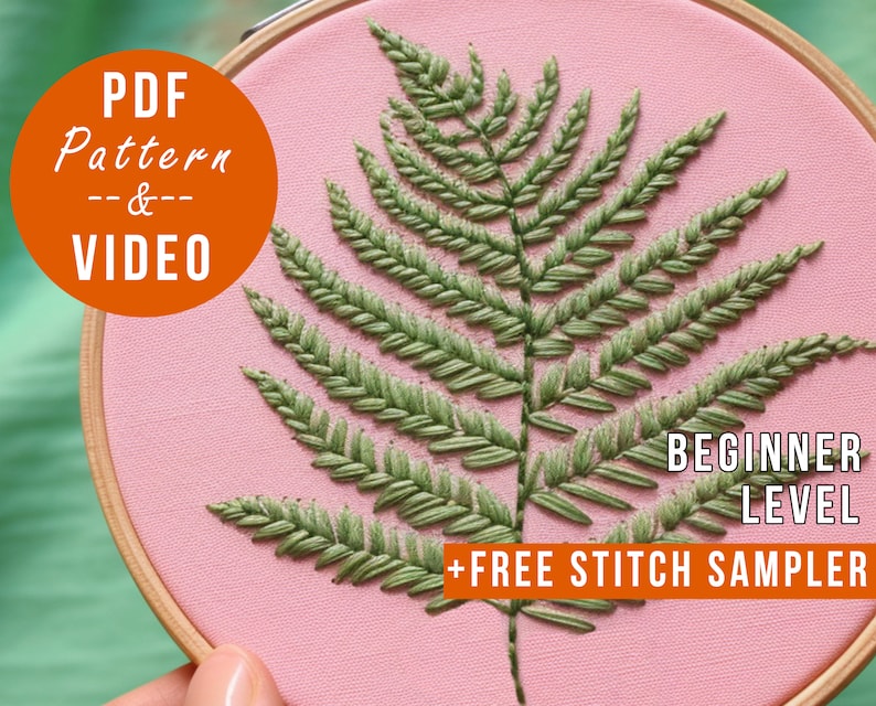 K&ouml;nnte beinhalten: Ein rosa Stickrahmen mit einem gestickten gr&uuml;nen Farnmuster. Der Text "PDF Pattern & VIDEO" befindet sich in einem orangenen Kreis oben links. Der Text "BEGINNER LEVEL + FREE STITCH SAMPLER" befindet sich unten am Rahmen in orange.