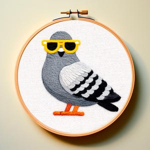 以下が含まれることがあります： 木製の刺繍枠に収められた、黄色のサングラスをかけた灰色のハトの刺繍アート。鳥は白と黒の羽のディテールとオレンジ色の足があり、すべて白い布にステッチされています。