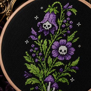 Könnte beinhalten: Ein runder Holzstickrahmen mit einem Kreuzstichmotiv auf schwarzem Stoff. Das Muster zeigt violette glockenförmige Blumen und eine violette Margerite, jeweils mit einem weißen Totenkopf in der Mitte, umgeben von grünen Blättern und kleinen weißen Sternen.