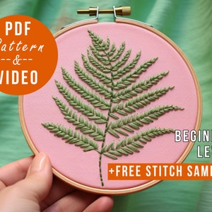 K&ouml;nnte beinhalten: Ein rosa Stickrahmen mit einem gr&uuml;nen Farnmuster. Der Rahmen ist mit "ANF&Auml;NGER-LEVEL" und "KOSTENLOSER STICHPROBEN-SET" beschriftet. Der Text "PDF-Muster & VIDEO" befindet sich in einem Kreis auf der linken Seite des Bildes.