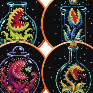 May include: Four circular wooden embroidery hoops containing cross-stitch patterns on black fabric. Each hoop features a different carnivorous plant inside a glass bottle or jar, rendered in vibrant colours like green, red, purple, and yellow.