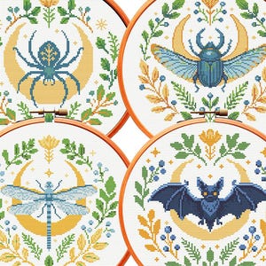 Op de afbeelding: Vier ronde houten borduurringen met kruissteekpatronen op witte stof. Elk ontwerp toont een centraal wezen—een spin, een kever, een libel en een vleermuis—omlijst door een gele halve maan en groene botanische elementen.