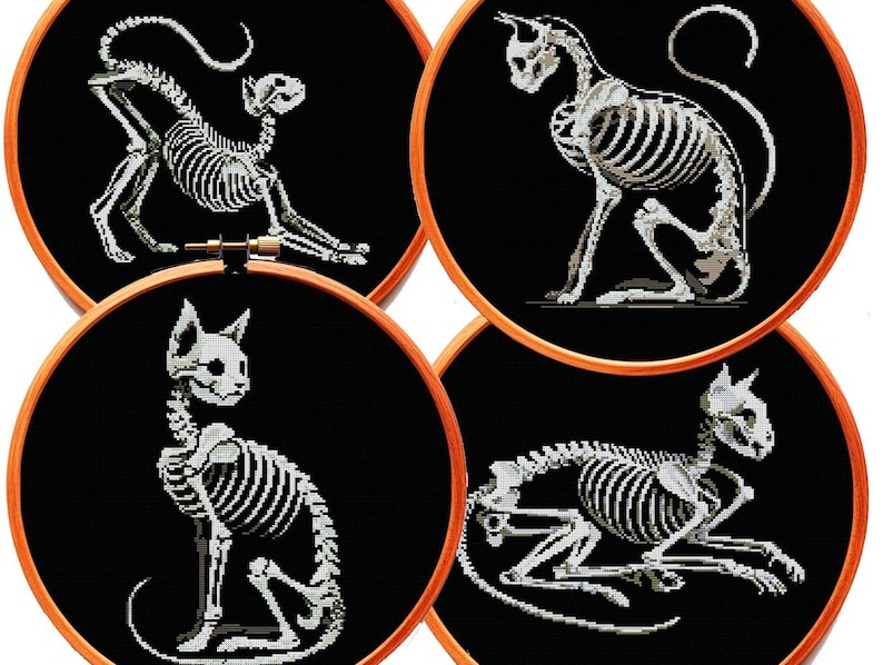 May include: Four circular wooden embroidery hoops containing black fabric with white cross-stitched cat skeleton designs. Each hoop displays a feline in a different pose: stretching, sitting upright, sitting alert, and lying down on the black fabric.
