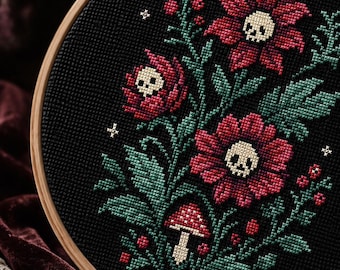 Può includere: Un telaio da ricamo circolare in legno contenente un motivo a punto croce su tessuto nero. Il disegno presenta fiori rossi con teschi color crema al centro, foglie verdi, piccole bacche rosse e un singolo fungo rosso e bianco.