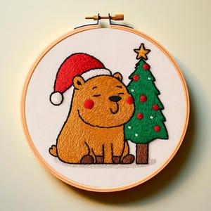 以下が含まれることがあります： 木製の刺繍枠に入ったクリスマスの刺繍。赤いサンタ帽をかぶった、笑顔の茶色いクマと、赤いオーナメントと金の星で飾られた緑のクリスマスツリーが描かれています。