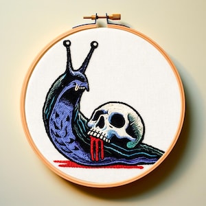 May include: Embroidered artwork in a wooden hoop. The design features a stylized, dark blue and purple snail with a skull. Red lines represent blood. The artwork is on a white background.