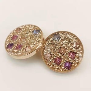 May include: Two gold-toned, round buttons with a mosaic of colorful square gemstones. The gemstones are arranged in a grid pattern, with hues of pink, purple, yellow, and blue. The buttons have a textured, ornate border.