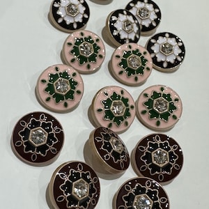 Peut inclure: Une collection de boutons décoratifs avec un motif floral. Les boutons présentent un strass central entouré d'une couleur contrastante, comme le noir, le blanc, le rose ou le marron. Les boutons ont un bord doré.