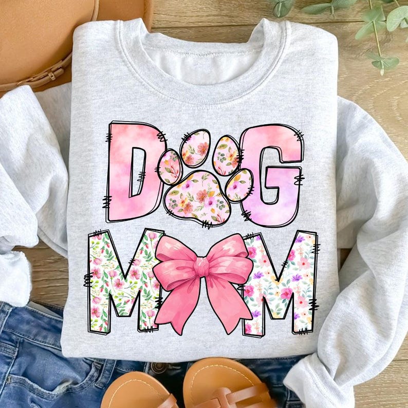 May include: A light gray sweatshirt with a pink and white floral design that says "Dog Mom" with a pink bow in the middle.