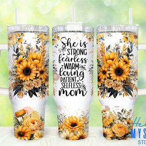 May include: A white tumbler with a floral design featuring sunflowers and roses. The tumbler has a black handle and the text "She is strong fearless warm loving patient selfless mom" is printed on the front.