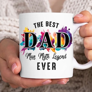 Op de afbeelding: Witte keramische mok met een kleurrijk aquarelontwerp en de tekst "The Best Dad Man Myth Legend Ever".