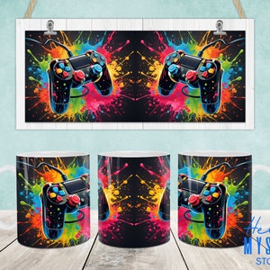 May include: Three white ceramic mugs with a black and colorful design of a video game controller with colorful paint splatters. The mugs are on a wooden surface.