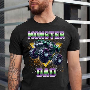 Puede incluir: Camiseta negra con un gr&aacute;fico de cami&oacute;n monstruo verde y el texto "Monster Dad" en morado y verde.