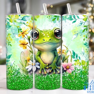 May include: A green frog with big eyes sits on a rock surrounded by green leaves and flowers. The background is a watercolor wash of green and blue. The image is on a green glitter tumbler.
