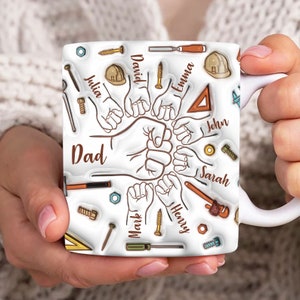 May include: White ceramic mug with a design of a group of hands forming a fist with the word "Dad" at the bottom. The hands are surrounded by tools and the names "David", "Emma", "John", "Sarah", "Mark", and "Henry".