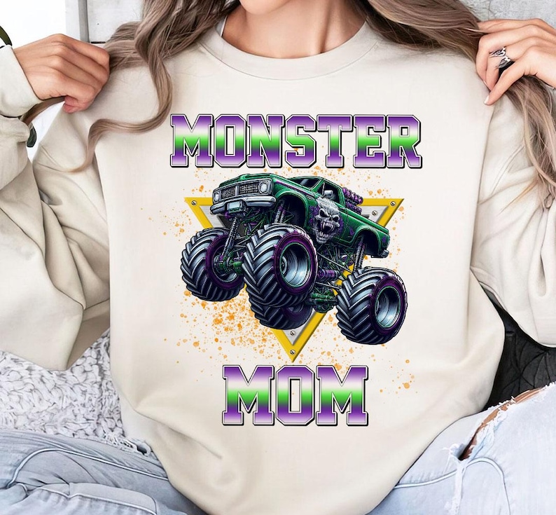 May include: A white sweatshirt with the text "Monster Mom" in purple and green letters. A green monster truck with a skull on the hood is in the center of the sweatshirt.